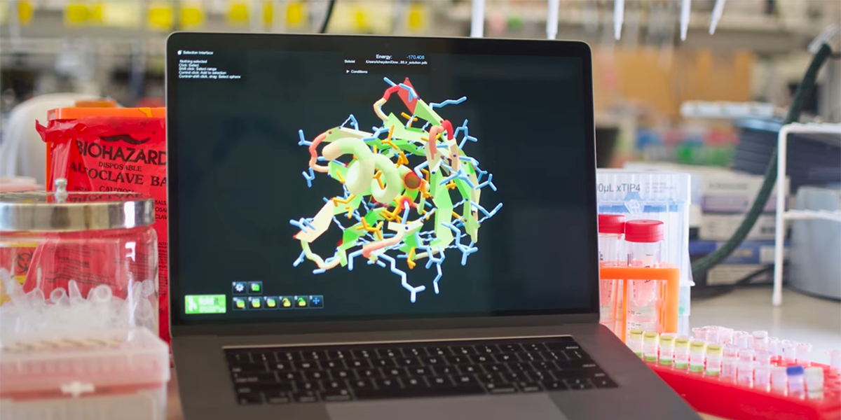 A laptop in a science lab with a protein molecule onscreen